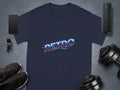 A navy blue T-shirt with a multicolored RETRO graphic from Garment Graphics exudes vintage charm. The classic fit piece is surrounded by a smartphone, smartwatch, black sneakers, portable speaker, and adjustable dumbbells on a gray surface.