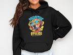 Wearing a Garment Graphics black hoodie, featuring the vibrant PAWSITIVE STYLISH design with a colorful dog graphic and sunglasses, a person smiles, their head partially out of view.