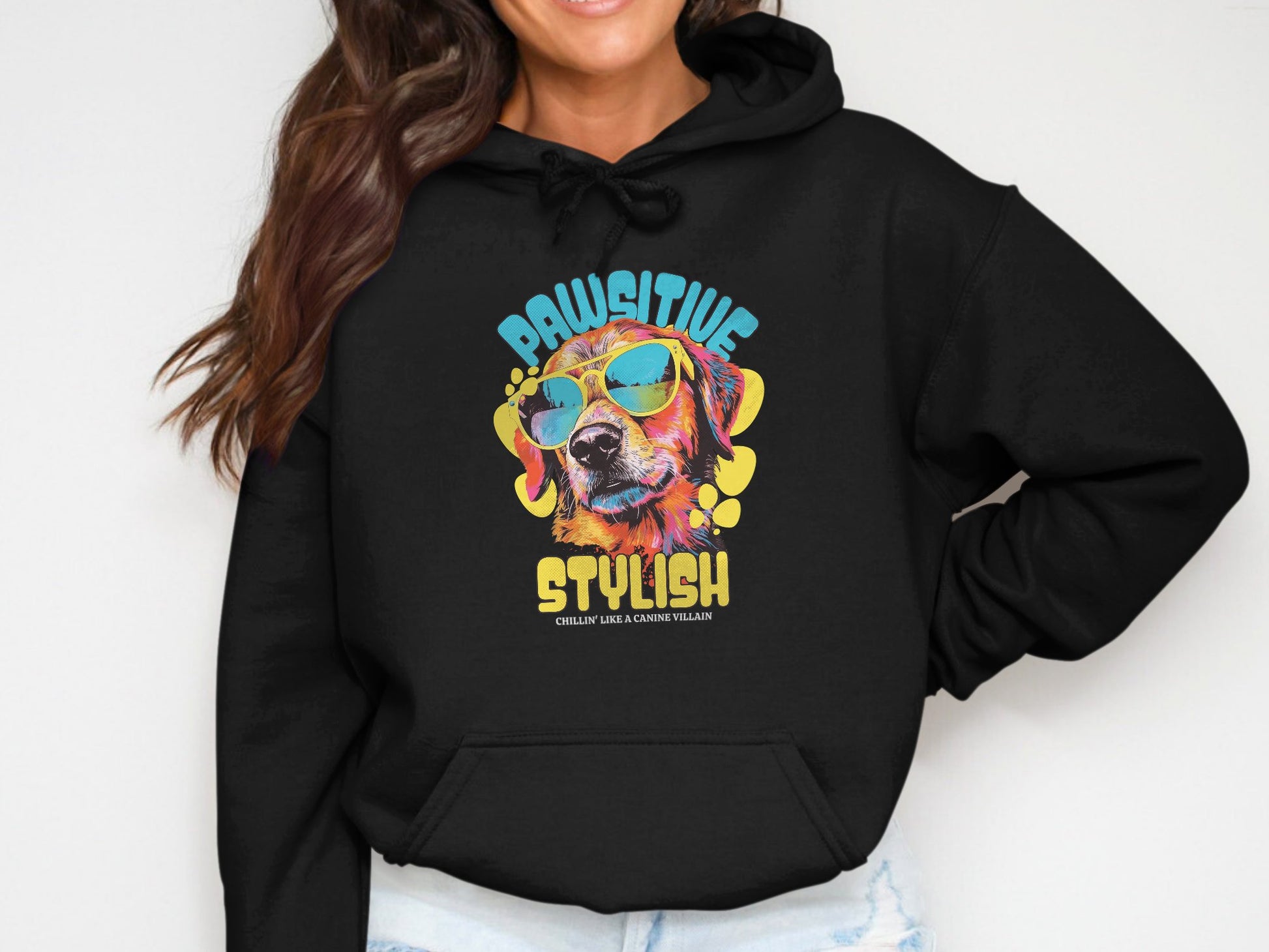 Wearing a Garment Graphics black hoodie, featuring the vibrant PAWSITIVE STYLISH design with a colorful dog graphic and sunglasses, a person smiles, their head partially out of view.