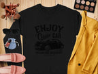 A Garment Graphics black sweatshirt with a Vintage Ride graphic is elegantly styled with a yellow blazer, pink shoes, sunglasses, makeup brushes, nail polish, and an eyeshadow palette on a rustic wooden surface.