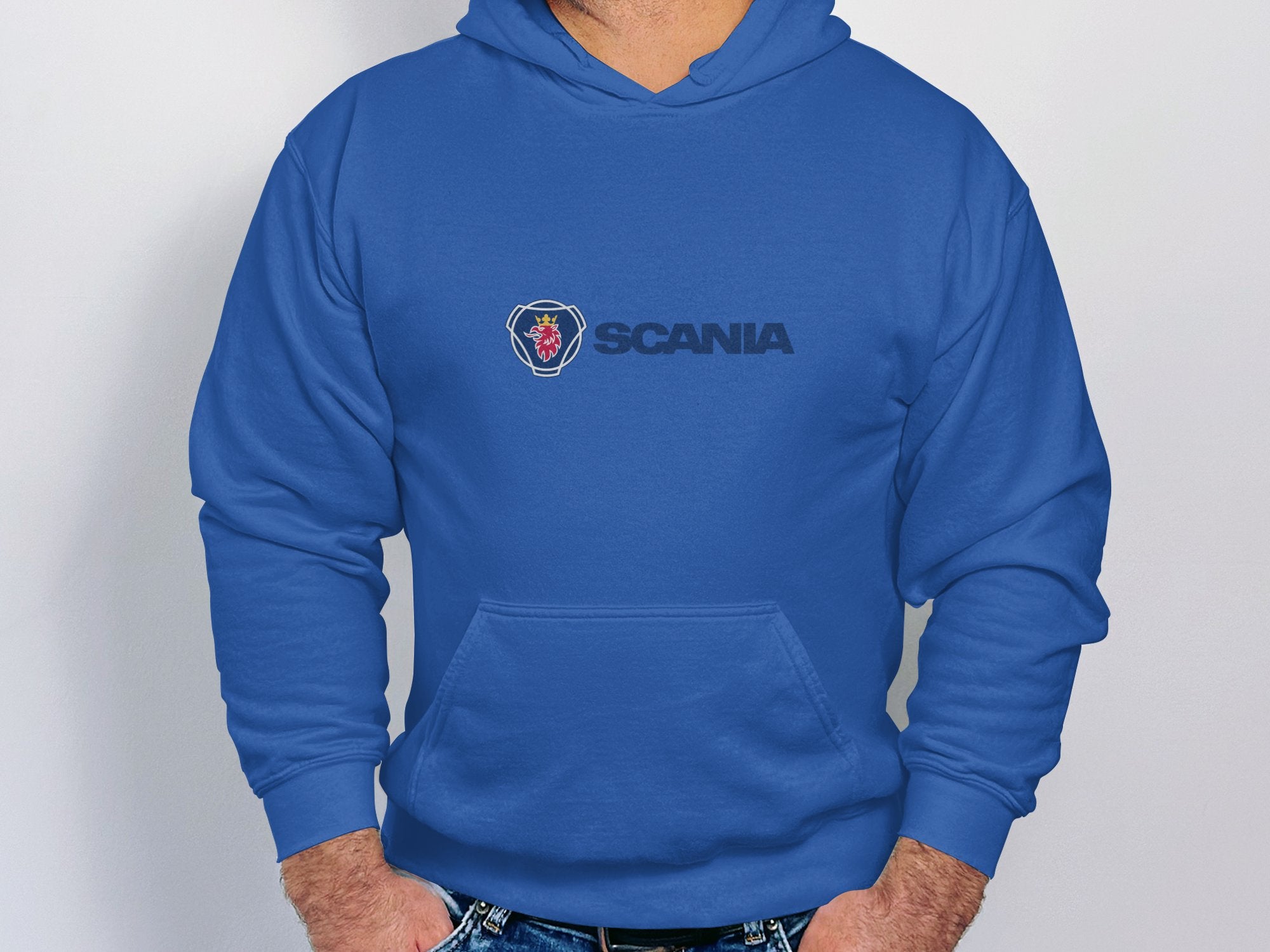 A person wearing a trendy blue Garment Graphics hoodie stands against a plain white wall, hands casually in the front pocket. This branded piece effortlessly combines style and comfort, making it a standout addition to any wardrobe.