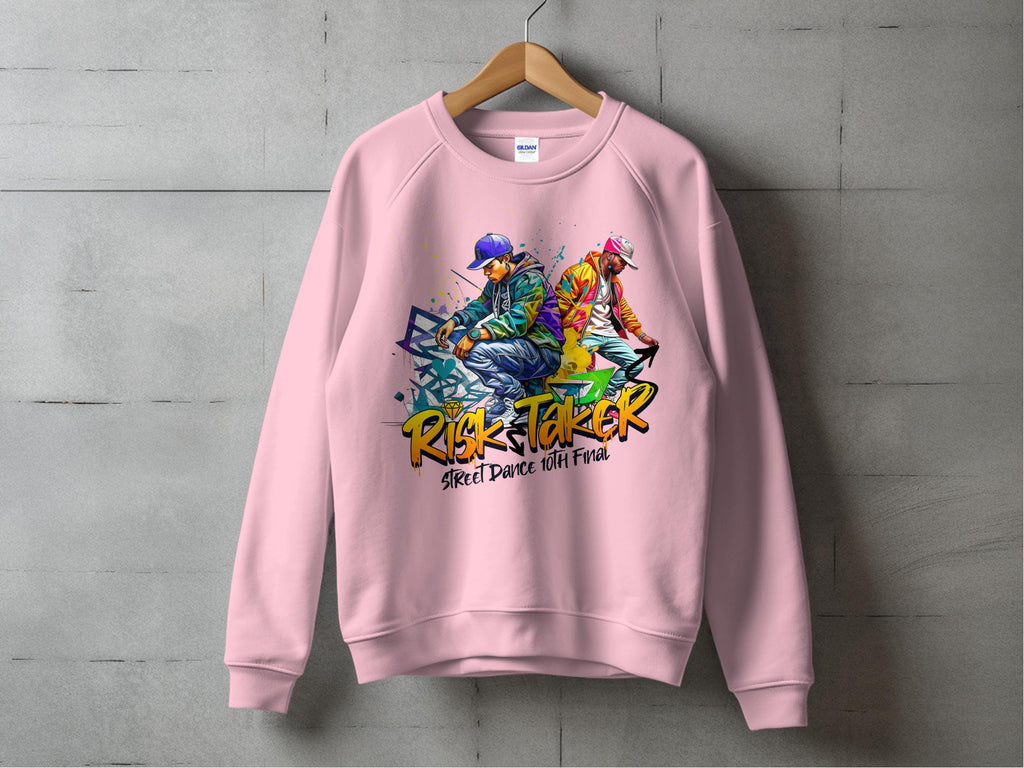 A pink sweatshirt from Garment Graphics features bold Risk Taker, Street Dance 10th Final text with vibrant street dance graphics of two people in dynamic poses wearing streetwear and caps. This urban style piece, in unisex sizing, is showcased against a concrete wall.