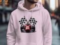 A person wearing a trendy white Garment Graphics hoodie, featuring a vivid red racing car and bold checkered flags design, stands in an outdoor setting amidst the blurred hustle of the city street.