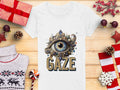 A Garment Graphics white graphic T-shirt features a jeweled eye design with GAZE lettering, set on wood. Surrounded by festive decorations like gifts, candy, and a sweater, this artistic T-shirt is available in womens sizes.