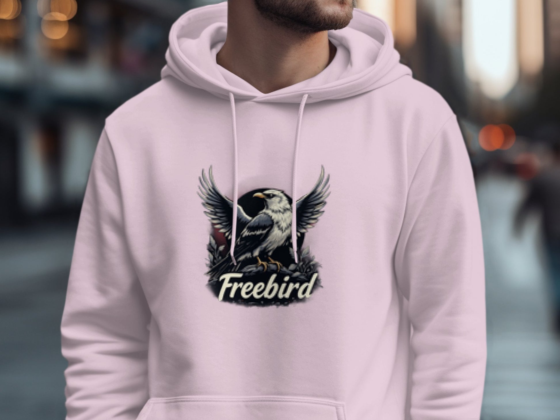 A person dons a light pink Freebird Graphic Pullover Hoodie by Garment Graphics on a city street. The eagle design adds flair, while the blurred backdrop of buildings and a passerby enhances the urban atmosphere.