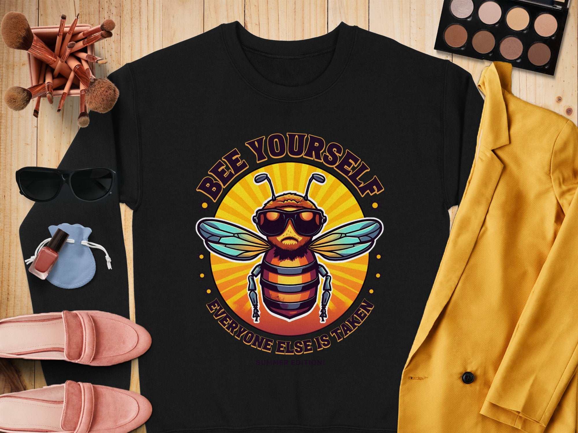 A black sweatshirt from Garment Graphics Summer Edition features a bee with sunglasses and Bee Yourself, Everyone Else is Taken. Perfect for pairing with womens accessories like a yellow jacket, sunglasses, makeup, shoes, and brushes on wood. Available in unisex sizing.