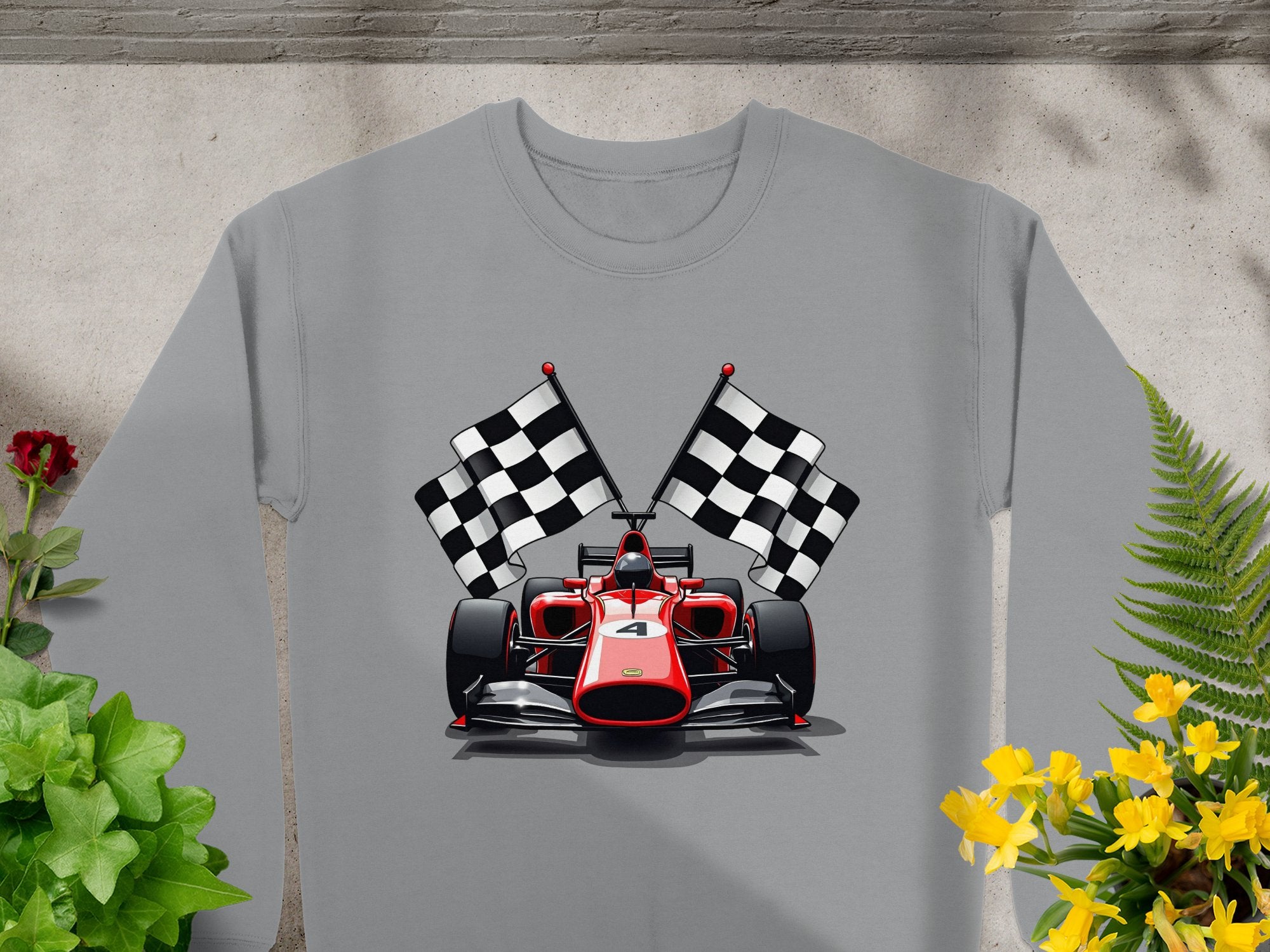 Garment Graphics presents a gray sweatshirt adorned with a red and black Formula 1 racing car and crossed checkered flags, ideal for motorsport fans. Vibrantly displayed on stone amid green plants and yellow flowers.