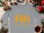 This whimsical gray Garment Graphics sweatshirt features bold orange FBI Female Boob Inspector lettering and unisex sizing, displayed among festive Christmas decorations like pine branches, ornaments, and a cozy cup of dark liquid on a wooden table.