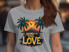 A person in a Garment Graphics t-shirt showcasing a colorful tropical sunset, two palm trees, a soaring bird, and One Love—ideal for the beach.