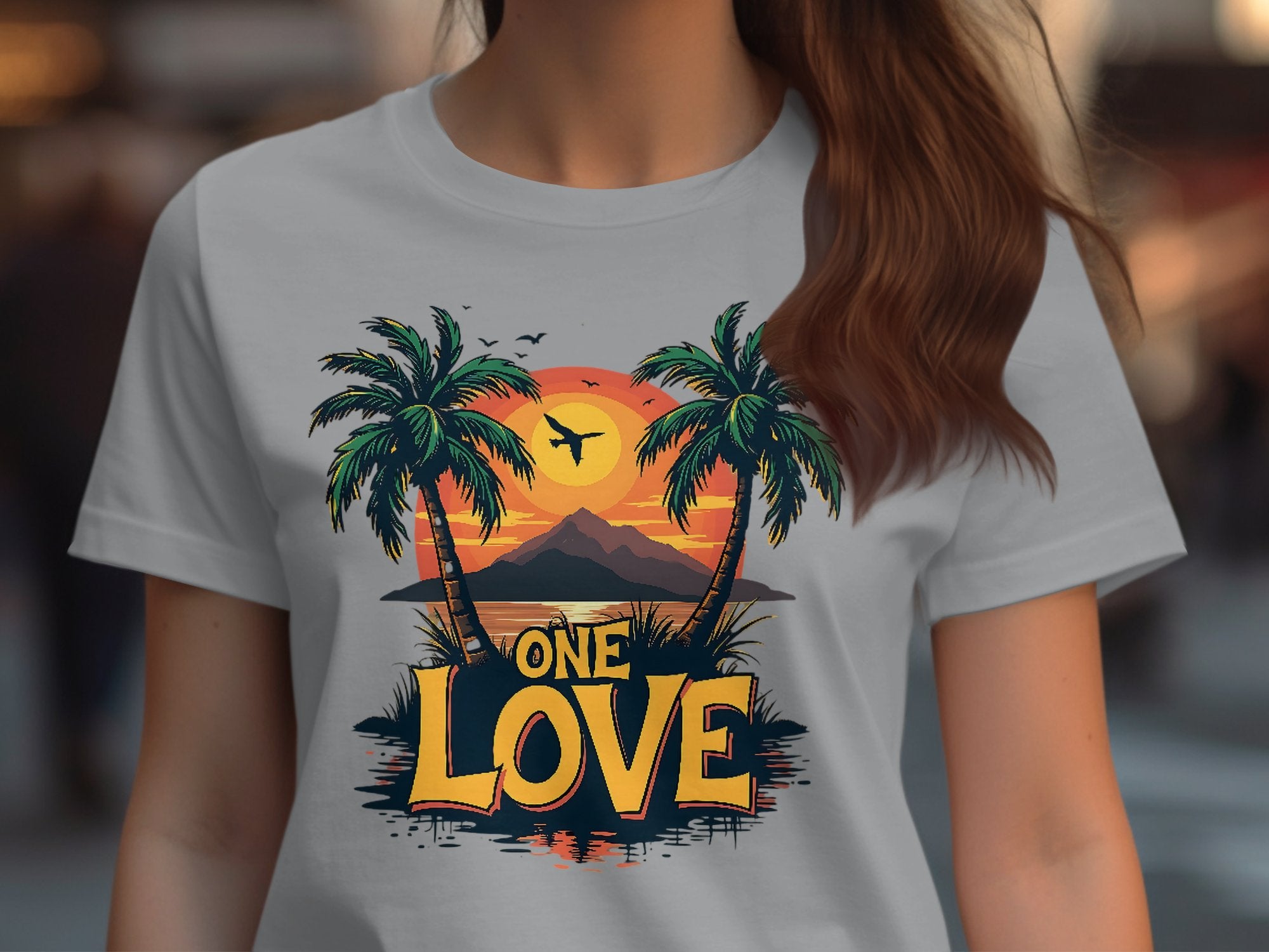 A person in a Garment Graphics t-shirt showcasing a colorful tropical sunset, two palm trees, a soaring bird, and One Love—ideal for the beach.