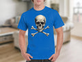 A person stands in a living room, making a bold fashion statement in a Garment Graphics blue graphic t-shirt with a prominent skull and crossbones design. The blurred background reveals cozy furniture and accents.