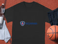 A black cotton T-shirt with the Scania logo by Garment Graphics rests on a sports court. A basketball is on the right with black shorts, while a partially seen white towel on the left holds a half-full water bottle—ideal for Scania fans.