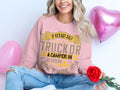 A person with wavy blonde hair sits on the floor wearing a Garment Graphics casual golf clubs sweatshirt with a playful message about golf, a truck, and a camper. Holding a red rose, they are surrounded by pink heart-shaped balloons.
