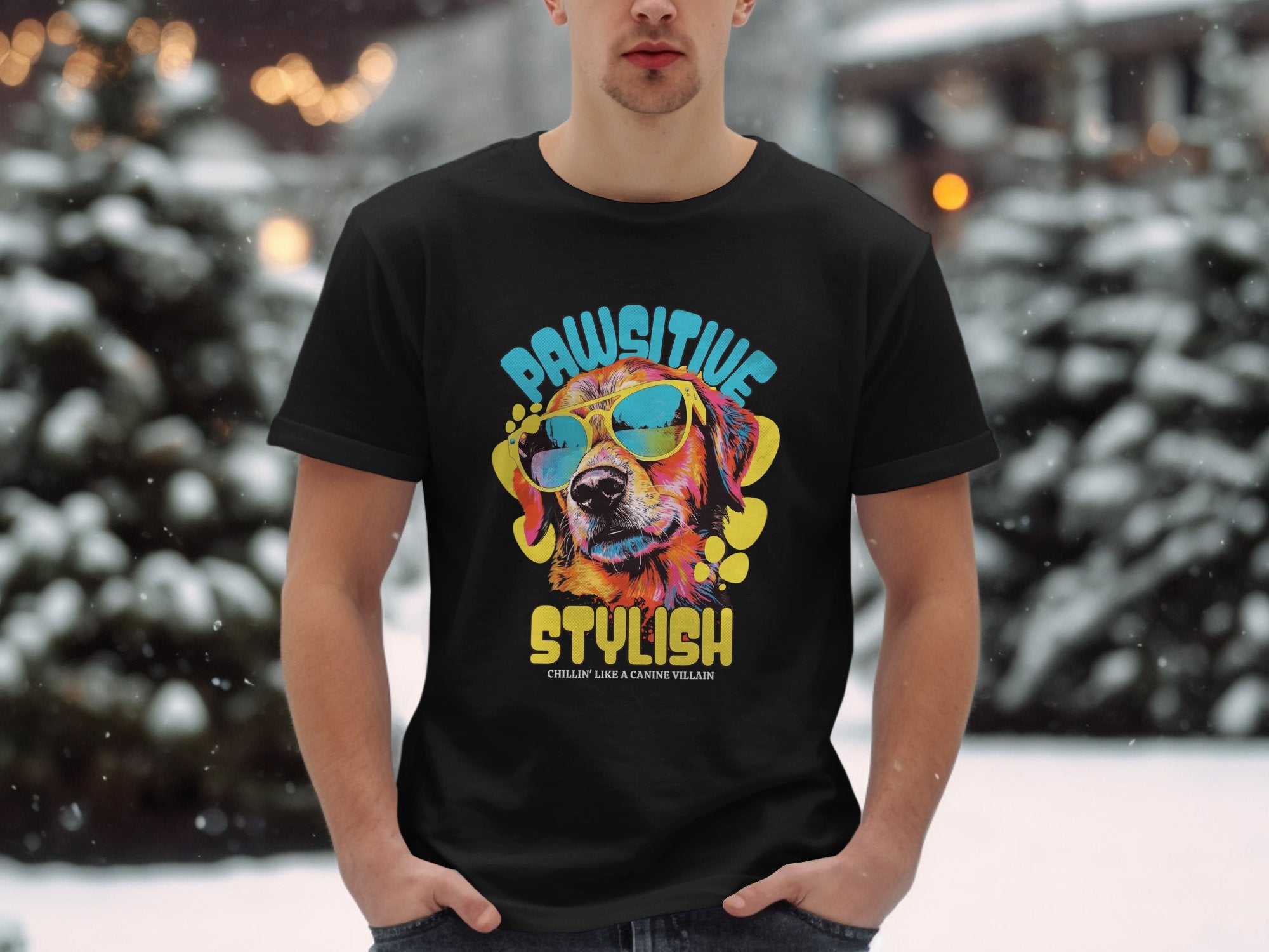 A person stands in a snowy landscape, wearing a black Garment Graphics Dog T-Shirt featuring a vibrant dog in sunglasses with Paw-sitive Stylish and Chillin Like A Canine Villain printed underneath.