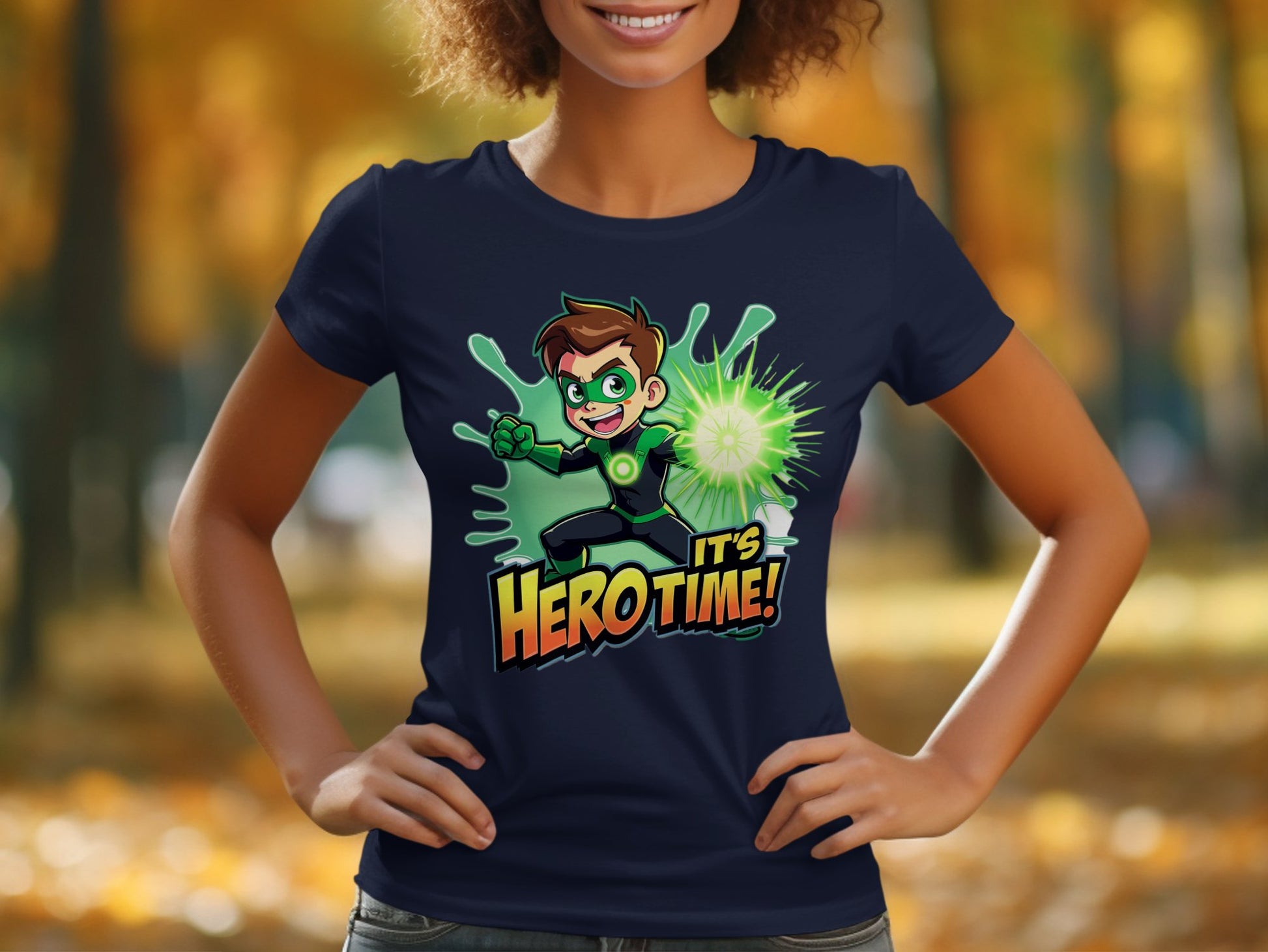 A person outside, against blurred autumn foliage, showcases a Garment Graphics navy blue T-shirt featuring an animated superhero with brown hair and a glowing green outfit. The shirt is emblazoned with the text Its Hero Time!.