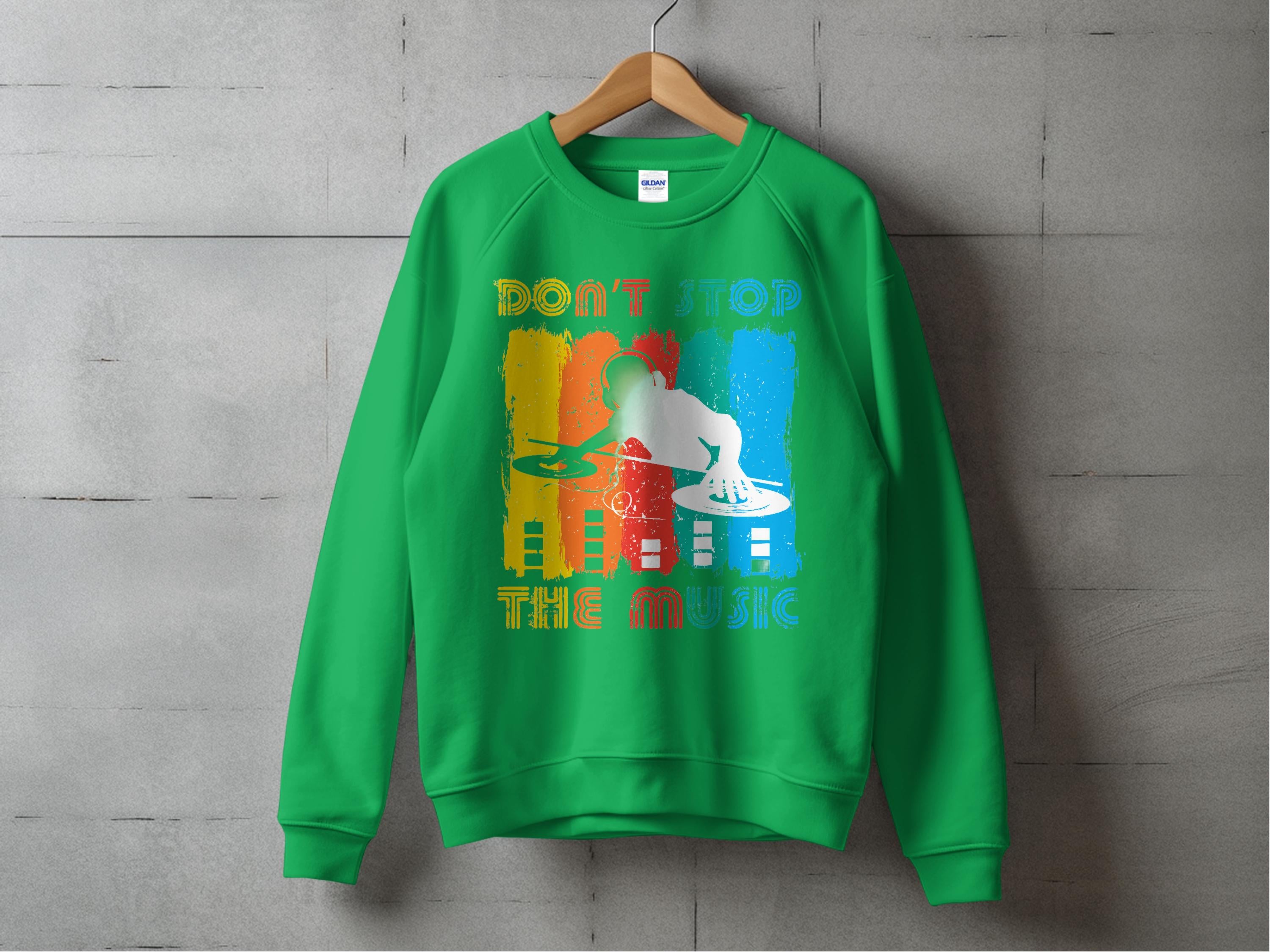 A green sweatshirt from Garment Graphics hangs against a concrete wall. This unisex design features a DJ silhouette with vibrant backgrounds and the phrase Dont Stop the Music, ideal for music enthusiasts.