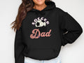 Wearing a stylish black hoodie from Garment Graphics, featuring Soccer Dad with the O as a soccer ball graphic, a person with long, dark hair poses confidently, hand on hip.