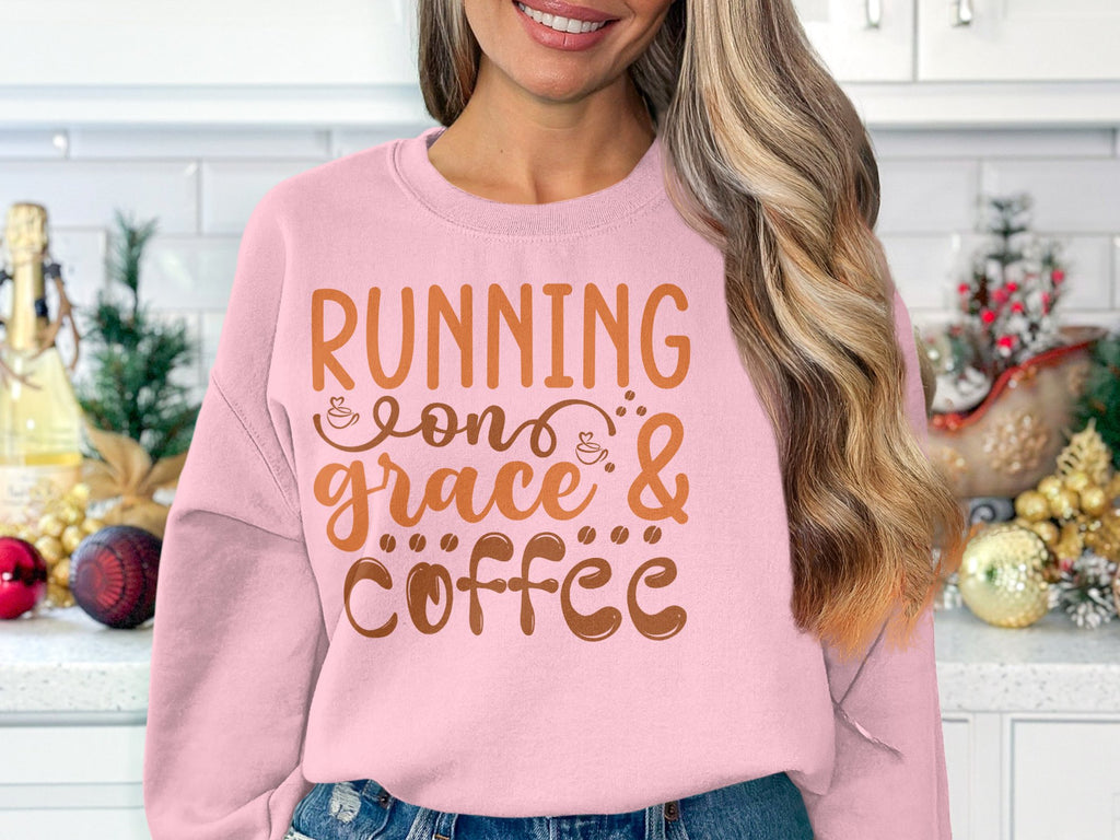 In a festive kitchen adorned with garlands and ornaments, a person wears Garment Graphics light pink sweatshirt emblazoned with Running on grace & coffee in brown. The unisex sizing guarantees comfort for everyone.