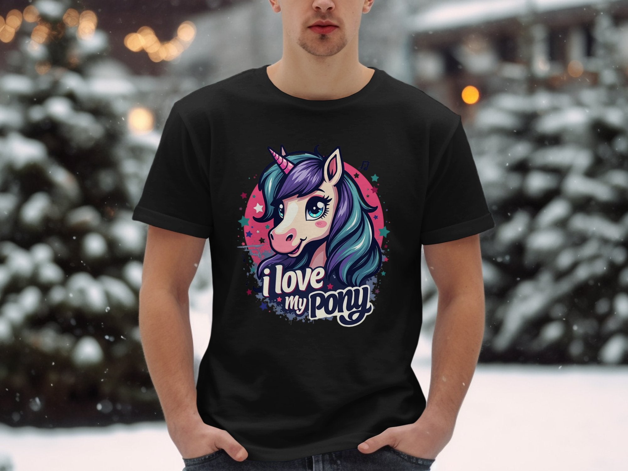 In a snowy outdoor setting, a person wears a black Garment Graphics Unicorn T-shirt with a vibrant pony graphic and the text I love my pony beneath it. Trees and snow form a picturesque backdrop for this unicorn enthusiasts standout piece.