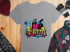 Garment Graphics gray t-shirt features a vibrant I Love Graffiti design with graffiti text and brick patterns, ideal for street art fans. Displayed on wood, it pairs well with a maroon knit hat, gray gloves, and a green plaid shirt.