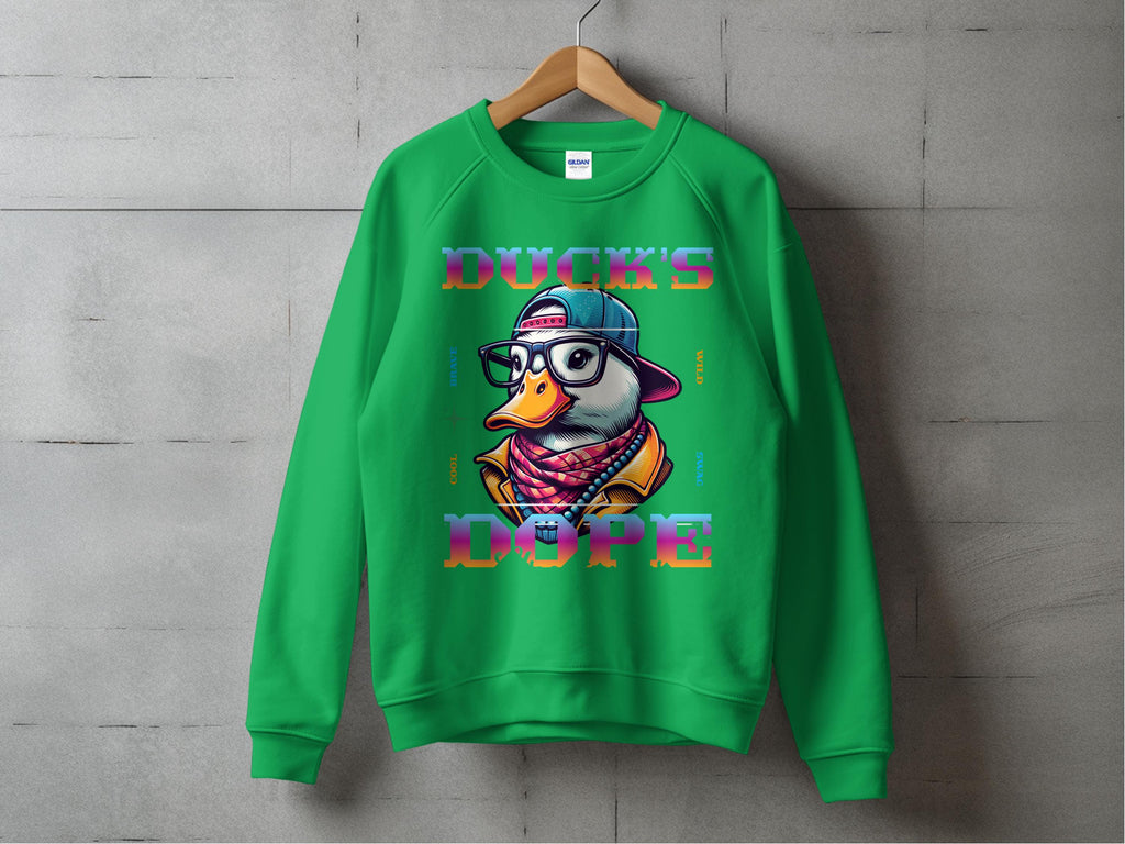 Garment Graphics presents a green sweatshirt with a cartoon duck in sunglasses, a backwards cap, and scarf, featuring DUCKS DOPE in bold letters. Made from medium-heavy fabric and unisex sized, its displayed on a wooden hanger against a concrete wall.