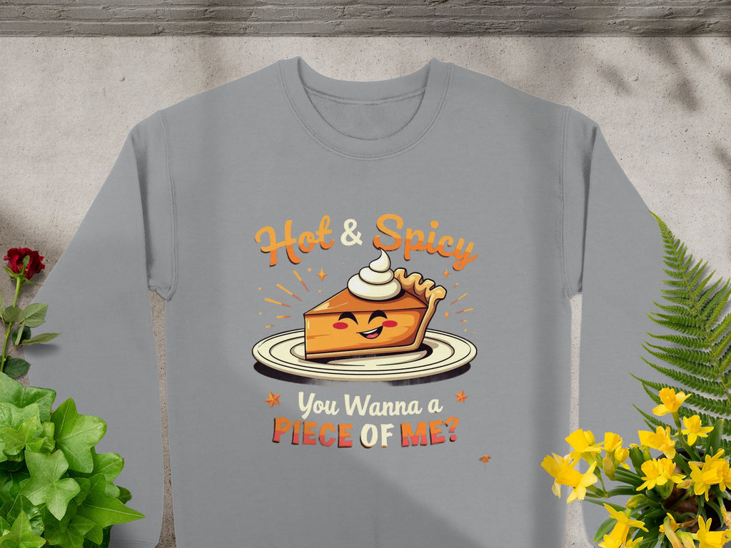 The Garment Graphics unisex sweatshirt showcases a playful pie graphic adorned with whipped cream and a smiling face, surrounded by Hot & Spicy and You Wanna Piece of Me? text, all set against green plants and yellow flowers.