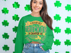 A woman in a humorous green Garment Graphics sweatshirt stands before shamrocks. Her shirt says, If hes got golf clubs in his truck or a camper in his driveway, I dont want him. Shes smiling, her long brown hair cascading over the playful design.