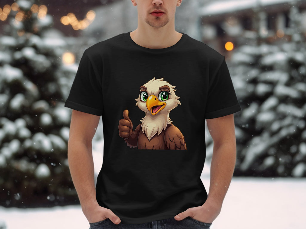 Dressed in a classic fit black Garment Graphics Eagle T-shirt showcasing a cartoon eagle giving a thumbs-up, the individual stands against a snowy backdrop with blurred trees and twinkling lights, enhancing the fun, casual vibe.