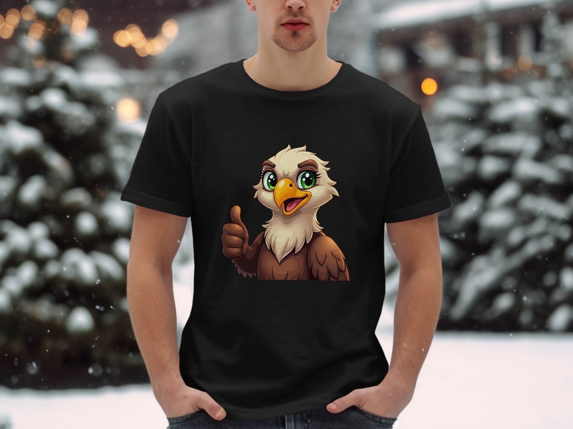 Dressed in a classic fit black Garment Graphics Eagle T-shirt showcasing a cartoon eagle giving a thumbs-up, the individual stands against a snowy backdrop with blurred trees and twinkling lights, enhancing the fun, casual vibe.