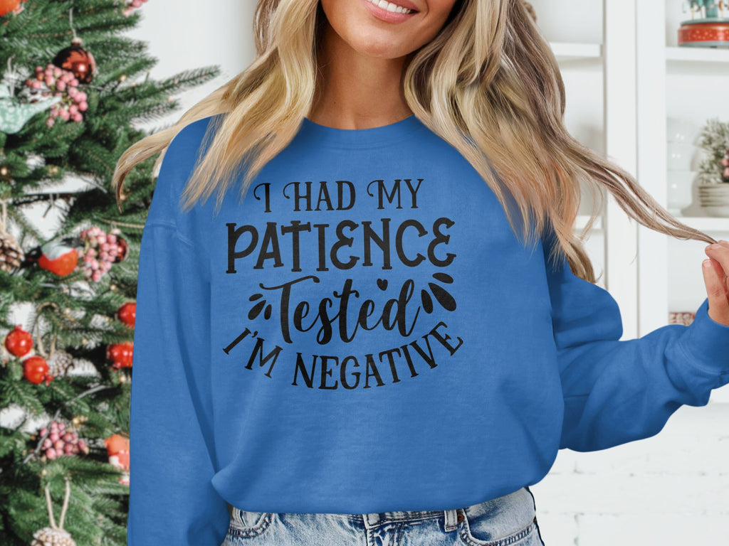 Indoors, someone wears a Garment Graphics blue sweatshirt with the humorous text I had my patience tested. Im negative. Its ideal for casual outings and pairs well with the festive atmosphere of the decorated Christmas tree in the background.