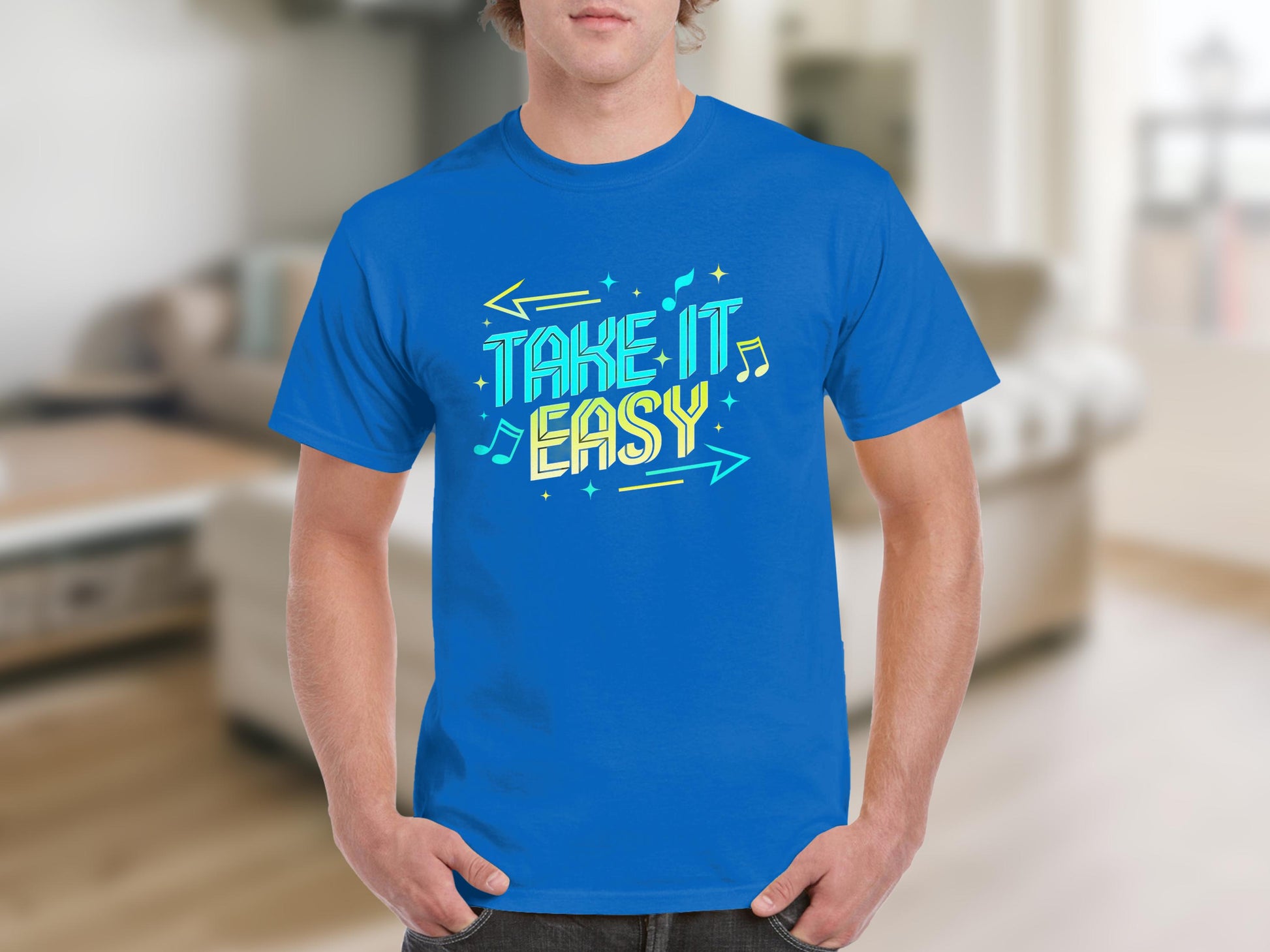 A person is wearing a vibrant Take It Easy T-shirt from Garment Graphics, showcasing colorful, stylized lettering with musical notes and arrow graphics set against a blurred indoor backdrop.
