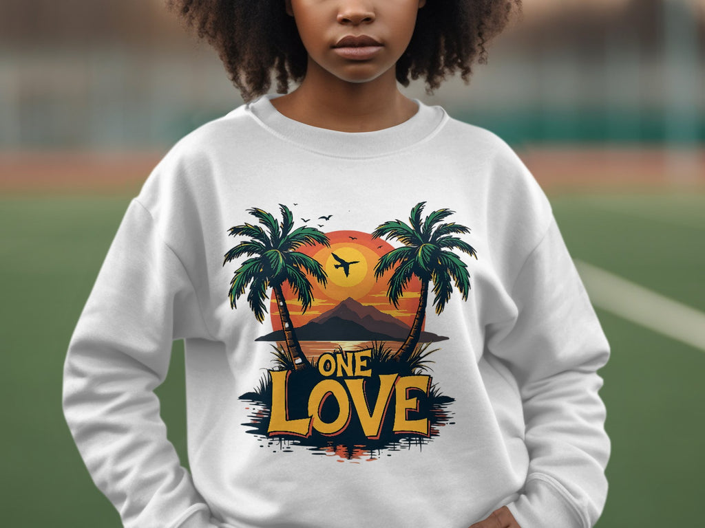 In front of a blurred backdrop, someone wears a vibrant white sweatshirt from Garment Graphics. This piece features a tropical design with palm trees and the stunning One Love Sunset, embodying the essence of relaxation and warmth.
