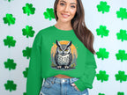 A person in a Garment Graphics green sweatshirt with an owl design stands against shamrock cutouts, wearing denim shorts that highlight the playful versatility of unisex sizing.