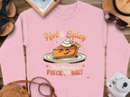 A pink Garment Graphics sweatshirt, featuring a smiling pie slice and the text Hot & Spicy You Wanna a Piece of Me? rests on wood near a camera, sunglasses, hat, shoes, and notebook. Perfect as a unisex option!.