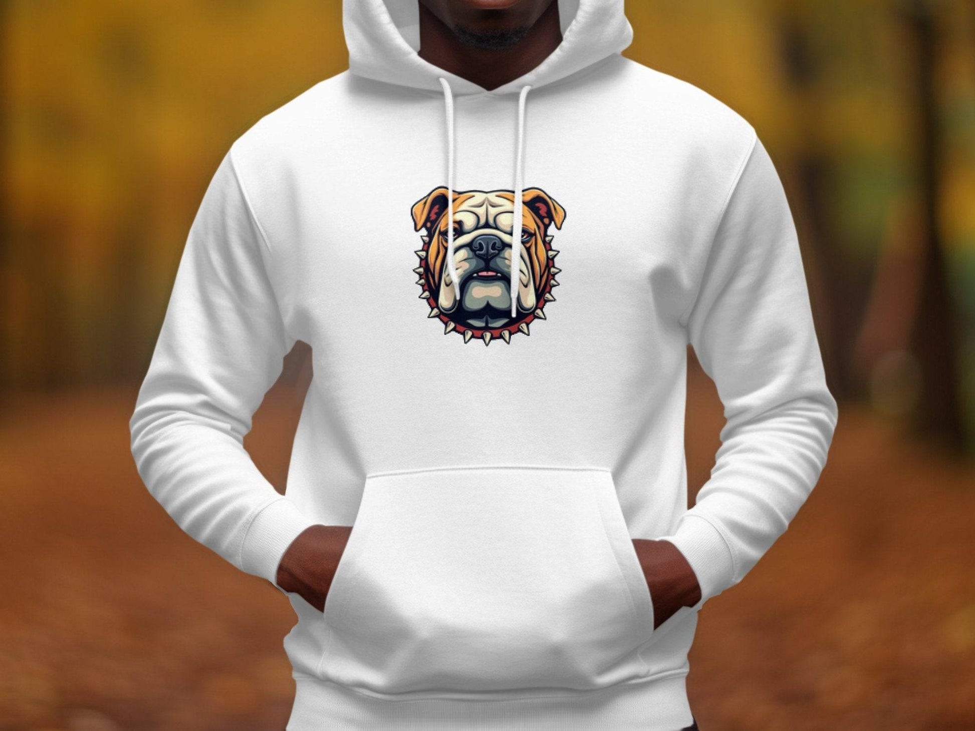 A person sports a Garment Graphics white hoodie, featuring a bold spiked-collar-style bulldog design. Their hands rest in the pockets against a blurred background of autumn foliage in yellow and brown hues.