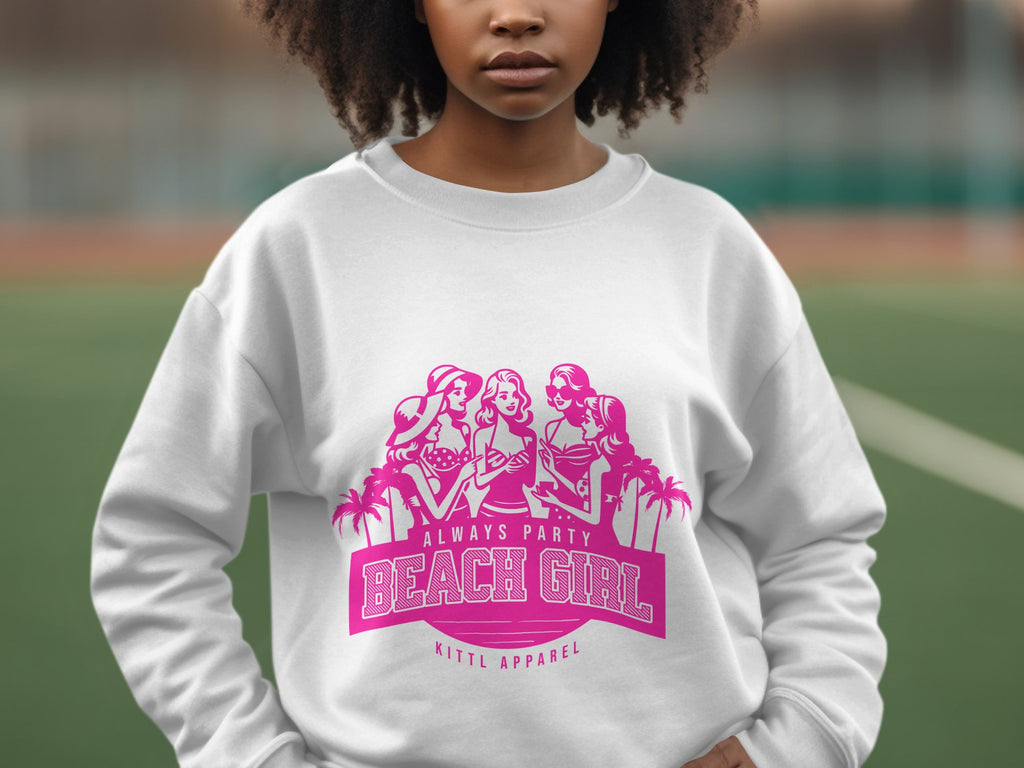 A person sports a white sweatshirt with a pink graphic of three illustrated women in beach attire. The text says Always Party Beach Girl and Garment Graphics, embodying laid-back fun. The backdrop suggests an outdoor sports court, enhancing the carefree vibe.