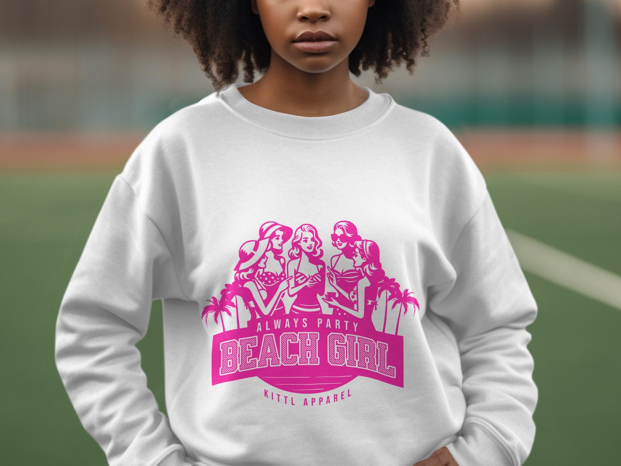 A person sports a white sweatshirt with a pink graphic of three illustrated women in beach attire. The text says Always Party Beach Girl and Garment Graphics, embodying laid-back fun. The backdrop suggests an outdoor sports court, enhancing the carefree vibe.