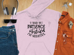 A light pink Patience Tested Hoodie by Garment Graphics, featuring I Had My Patience Tested, Im Negative, rests on wood. The medium-heavy fabric offers warmth, accompanied by headphones, black sunglasses, jeans, an orange shirt, watch, and keys.