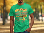 A man in a Garment Graphics green T-shirt with the funny quote If hes got golf clubs in his truck or a camper in his driveway, dont hire him. stands amid trees with fall leaves, setting the perfect backdrop for this humorous moment.