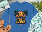 A Garment Graphics blue sweatshirt with palm trees, a sunset, and One Love Sunset text is pictured with sandals, a green striped shirt, a wristwatch, a fern leaf, and a blue handbag on a gray surface.