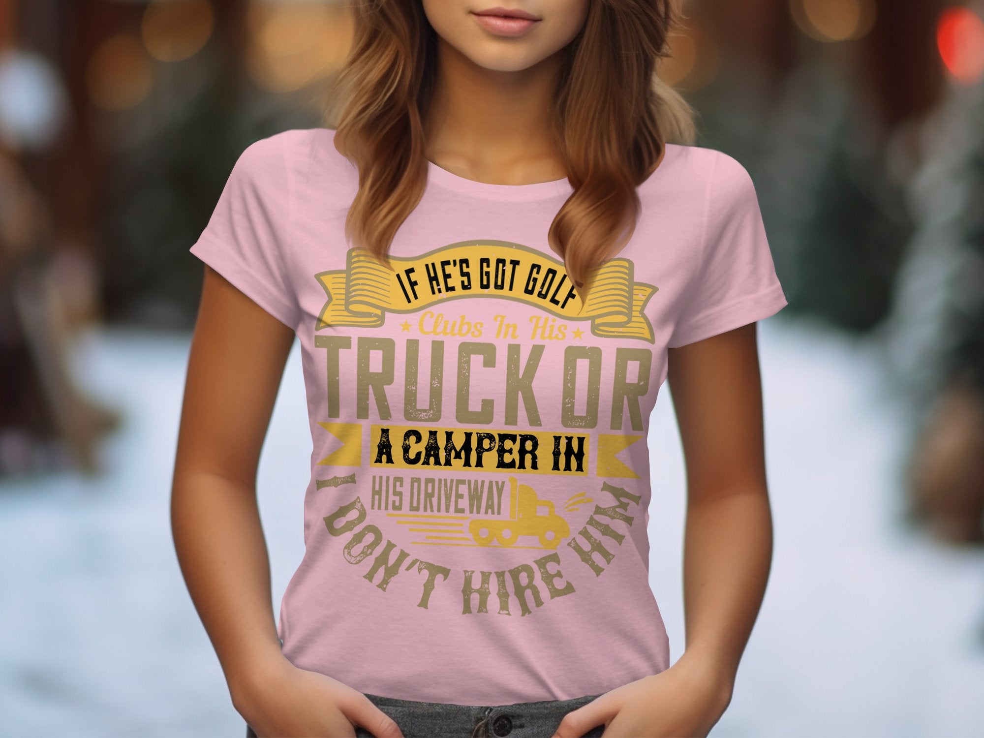A person wears a Garment Graphics pink womens T-shirt with the quirky text, If hes got golf clubs in his truck or a camper in his driveway, I dont hire him. The background is blurred with greenery and abstract shapes.