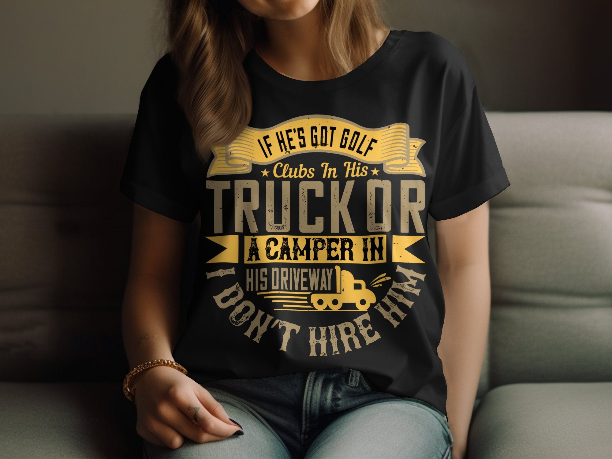 A person wears a black Garment Graphics T-shirt in womens sizing, featuring the humorous message, If hes got golf clubs in his truck or a camper in his driveway, I dont hire him! The quirky design includes yellow and white lettering with a small camper graphic.