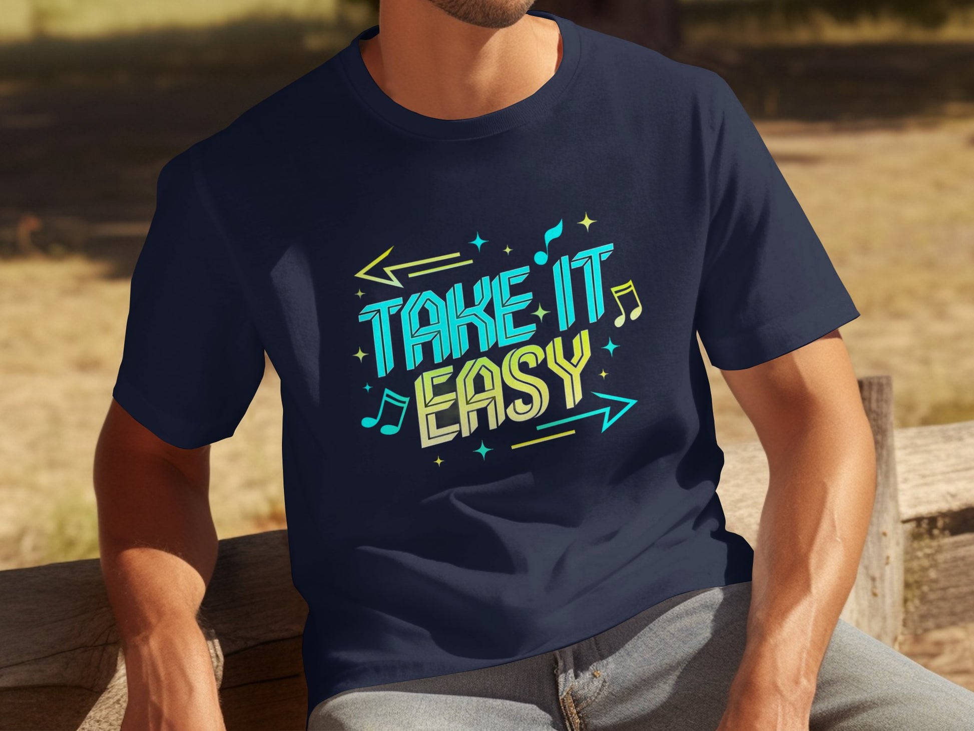 An individual is seated on a wooden bench outside, wearing a navy blue Garment Graphics Take It Easy T-shirt. The shirt features colorful, stylized text with musical notes and arrows, though the persons face isnt visible.