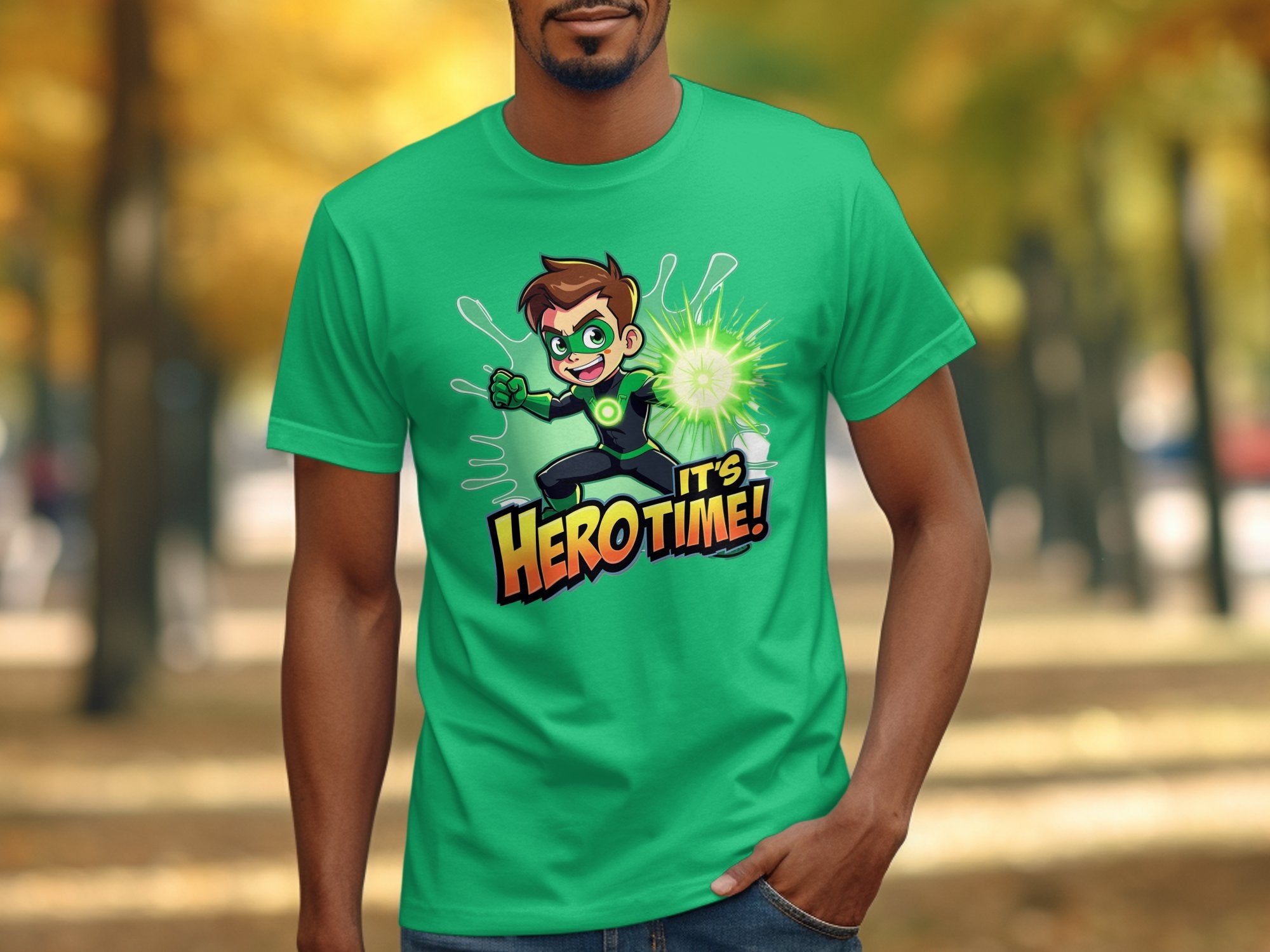 Someone sports a lively green Garment Graphics t-shirt featuring a superhero graphic and Its Hero Time! text. Ideal for family-sized adventures, the tee is set against an outdoor scene with trees and fallen leaves.