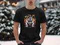 A person outdoors in snowy surroundings, with blurred evergreen trees and warm lights in the background, wears a Garment Graphics black t-shirt featuring a unique bulldog design and the words City King.