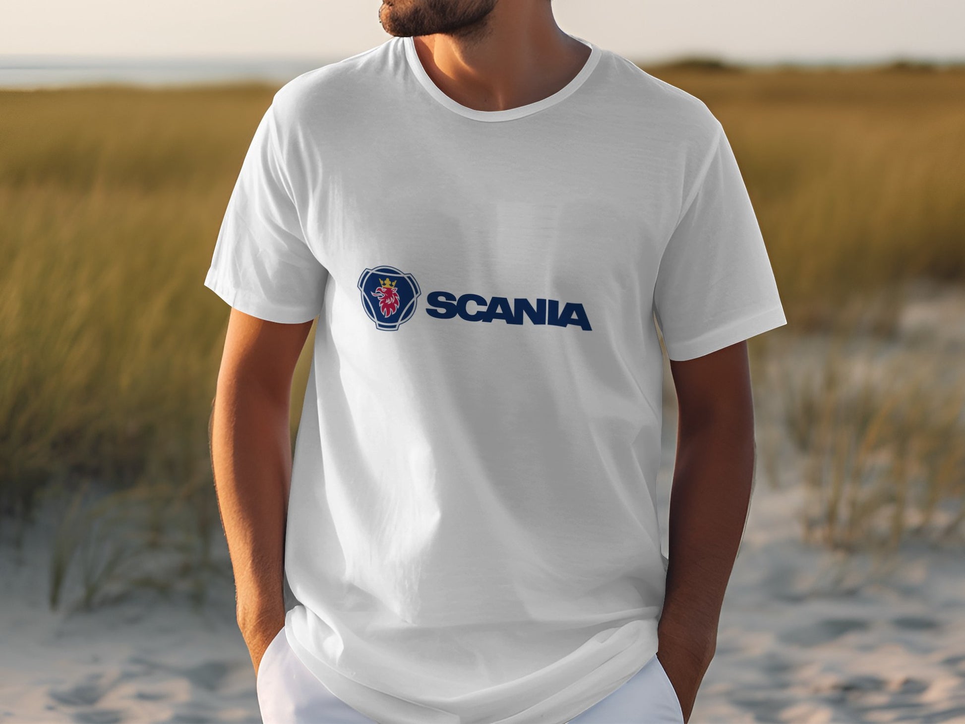 Amidst a sandy landscape with grass, someone wears a stylish white cotton T-shirt branded Garment Graphics, emblazoned with the Scania logo.