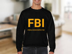 Wearing a Garment Graphics black sweatshirt with bold yellow FBI and Female Boob Inspector text, a man confidently stands in a room with a blurred background. The unisex sizing ensures a comfortable fit.