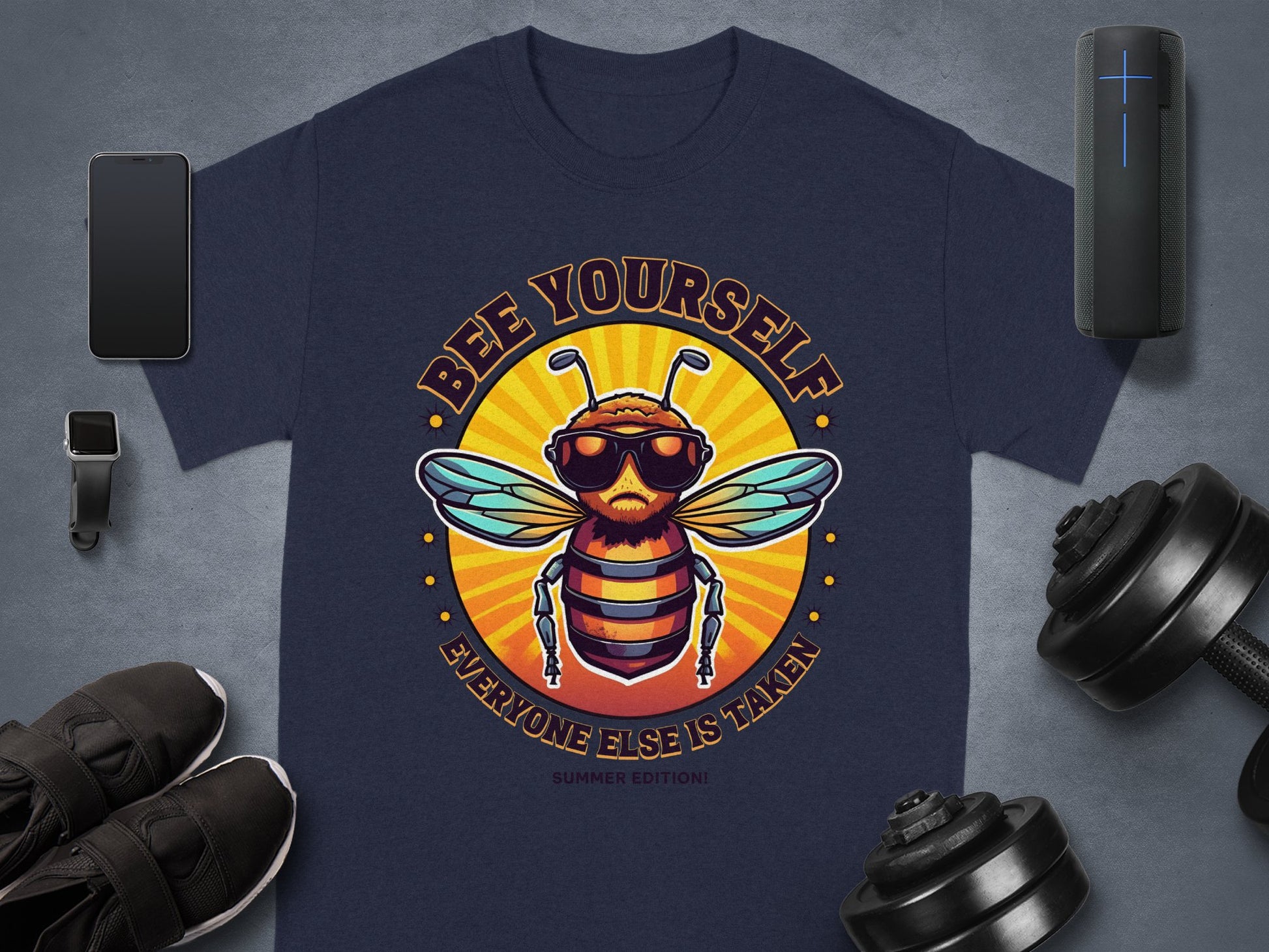 Navy T-shirt by Garment Graphics displays a stylish bee in sunglasses with Bee Yourself, Everyone Else Is Taken text in a circular design. Its surrounded by a smartphone, smartwatch, sneakers, dumbbells, and speaker on gray. Part of the family-friendly Every One Else Is Taken collection.