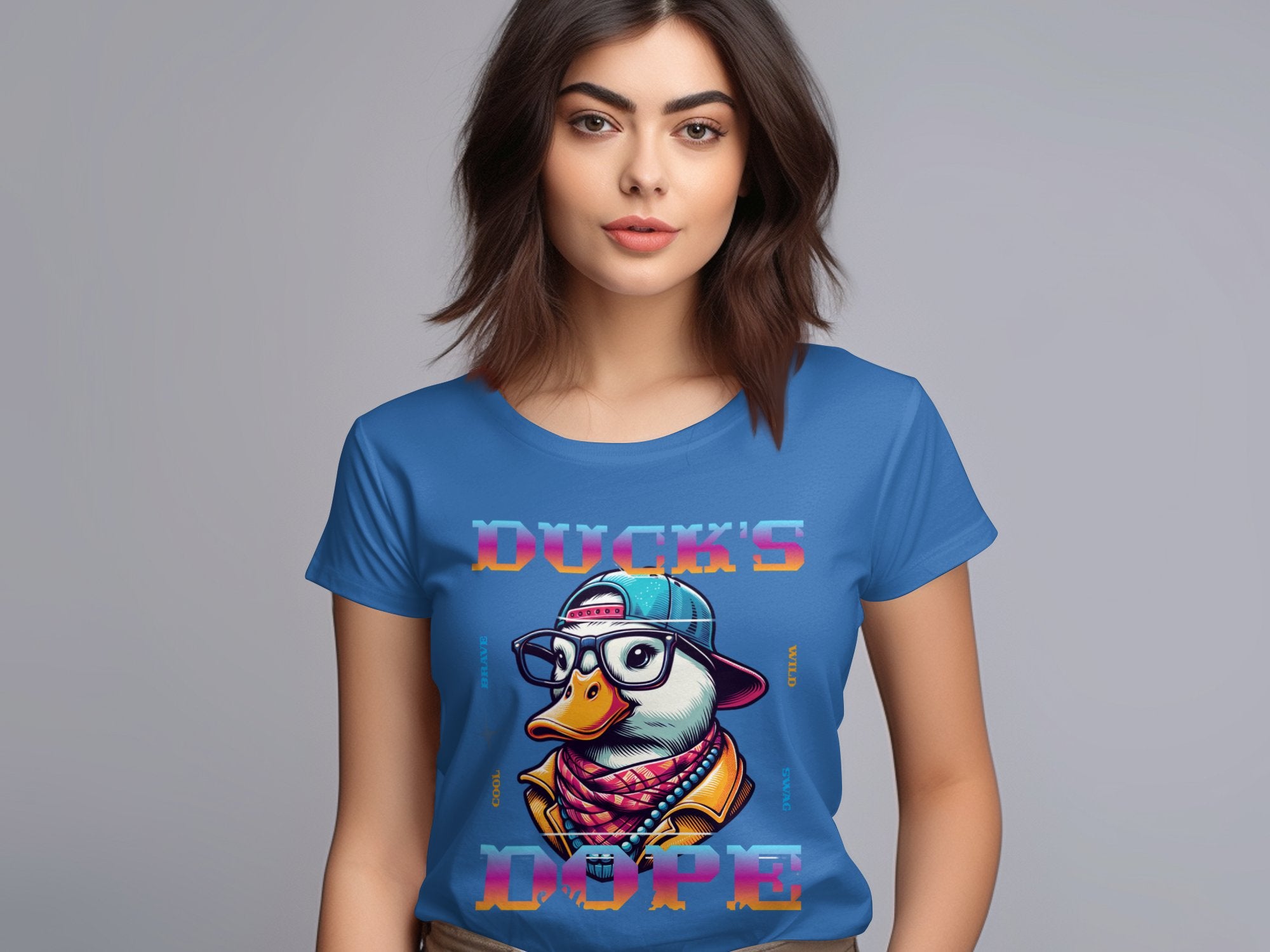 A woman with shoulder-length brown hair wears a blue T-shirt by Garment Graphics, featuring a cartoon duck wearing glasses, a cap, and a patterned scarf. The shirt reads DUCKS DOPE in colorful letters, capturing the Cool Brave Wild Swag Duck vibe through its unique design.