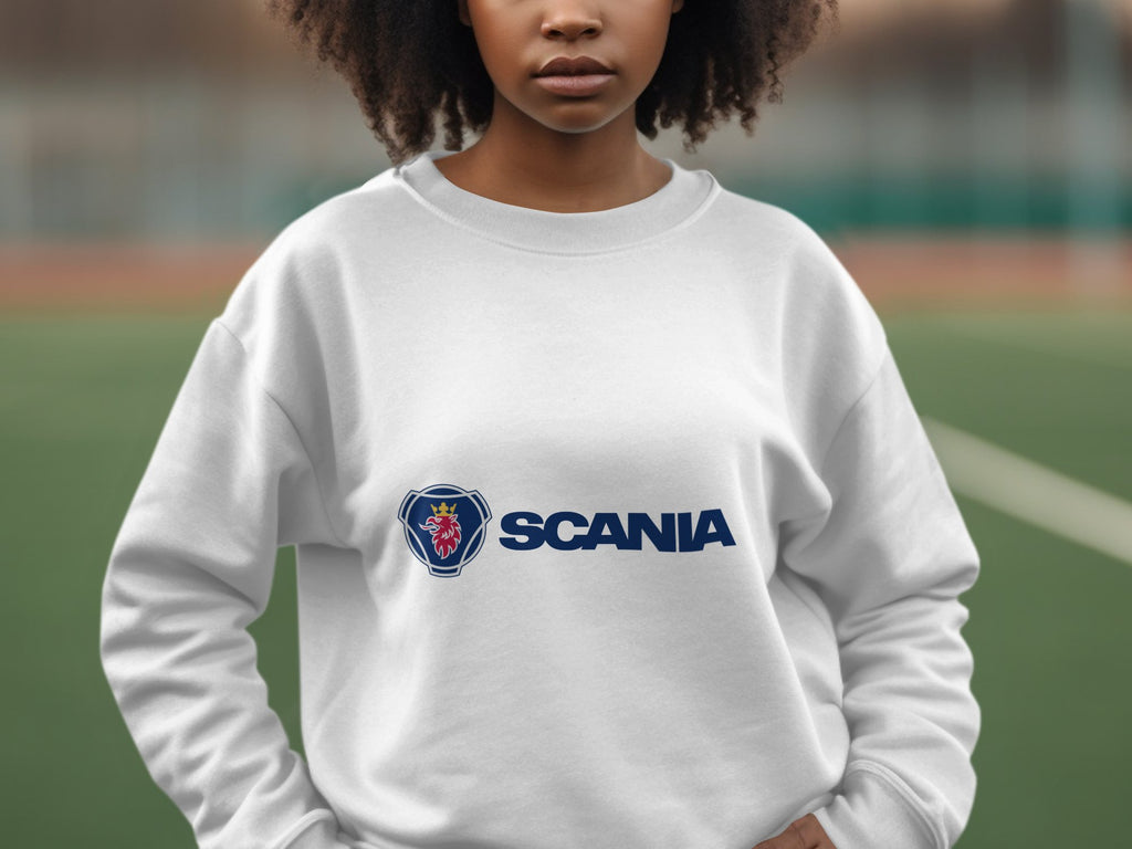 On a sports field, someone wears a unisex white sweatshirt from Garment Graphics featuring a prominent Scania logo, with the blurred background suggesting leisurely outings.